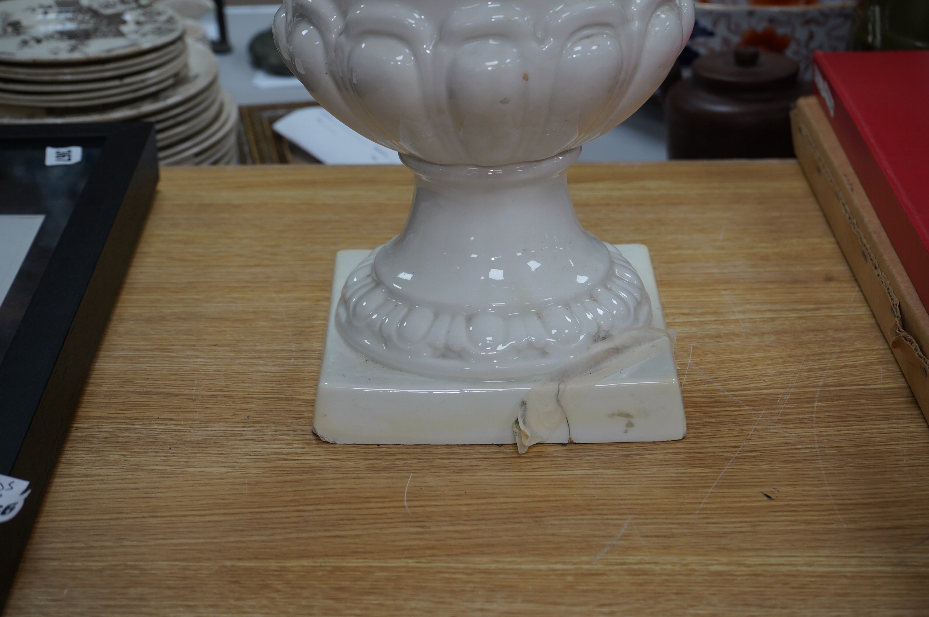 A large cream glazed pottery pedestal vase, with decorative swag of fruit and leaves, 43cm high. Condition - corner of square base broken, glazing chipped on top rim and fruit and leaf decoration broken